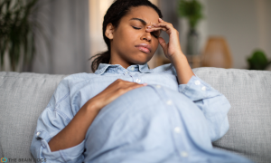 Pregnant woman on a couch in clear mommy brain discomfort.