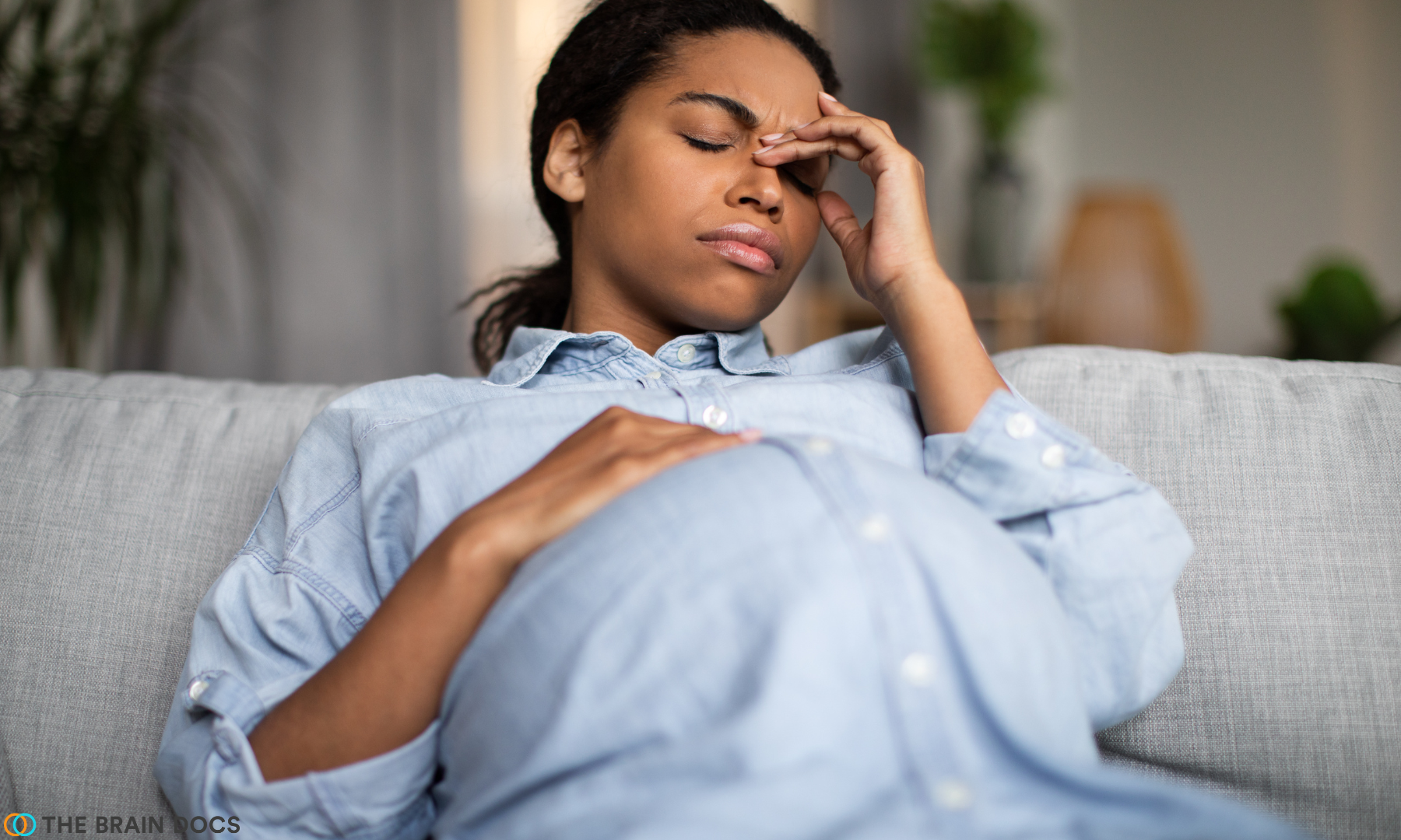 Pregnant woman on a couch in clear mommy brain discomfort.